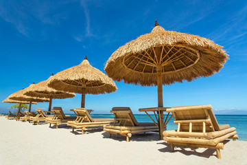 Beach chairs with straw umbrellas on a beautiful tropical beach..
