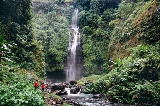 Huge Active Waterfall In Green Tropical Mountain Forest With People Watching Its Flow In Bali.