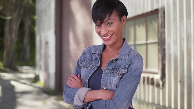 Confident millennial woman with arms crossed wearing jean jacket. Happy smiling black woman in her 20s.