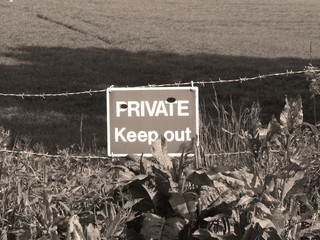 Sepia private keep out sign on barbed wire boundary fence to farmland
