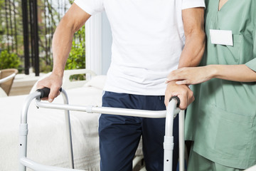 Nurse Assisting Senior Man With Walker In Rehab Center