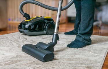 Man is cleaning carpet with vacuum cleaner.