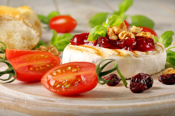 Grilled brie cheese with cranberry jam and walnuts on white wood