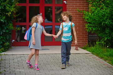 Little school students go on a schoolyard holding hands.