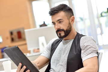 Trendy bearded guy in office websurfing on tablet