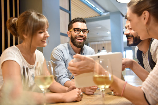 Young people in bar looking at pictures on tablet