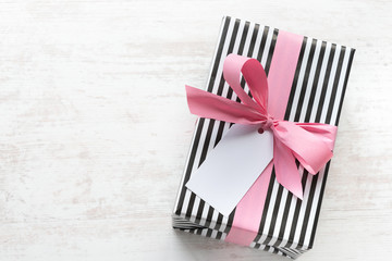 Gift box wrapped in black and white striped paper with pink ribbon on a white wood old background....