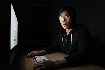 Fototapeta na wymiar Amazed asian young man working with computer in dark office
