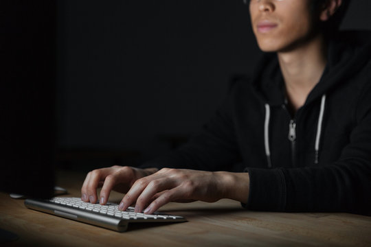 Serious asian young man typing on keyboard in dark room