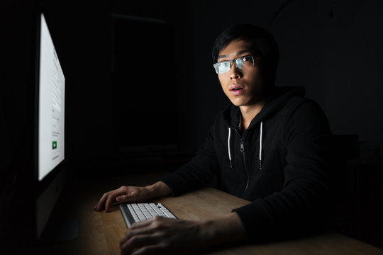 Amazed asian young man working with computer in dark office