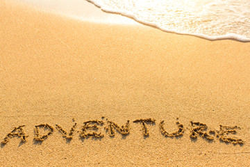 Adventure - word drawn on the sand beach with the soft wave.