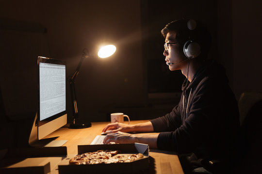 Man working with computer and eating pizza in dark office