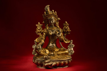 Statuette of Green Tara on a red background.