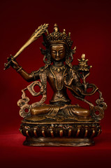Statuette of Manjushri on a red background.