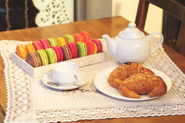 French colorful macarons in a box, croissants, cup and teapot