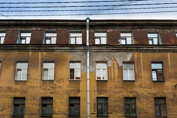 Yellow classic old dirty house with penthouse and crumbling plaster.