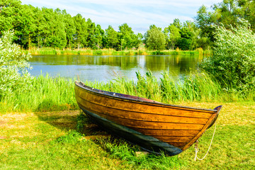 Obraz premium Very fine open wooden rowboat lying on land beside the water in the background. Afternoon sunlight and fine summer nature.