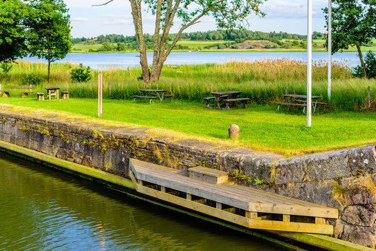 Mooring place in a canal with a wooden bridge or jetty and a granite bollard in the grass beside the waterway. Gota canal at Mem in Sweden.