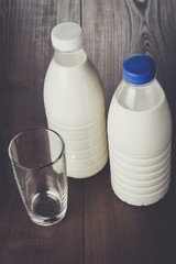 empty glass and two bottles of milk on wooden table