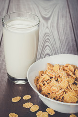 glass of milk and bowl with cornflakes on the table