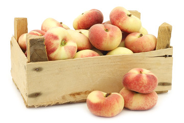 fresh colorful flat peaches (donut peaches) in a wooden crate on a white background