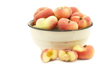 fresh colorful flat peaches (donut peaches) in an enamel bowl on a white background