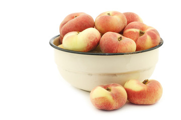 fresh colorful flat peaches (donut peaches) in an enamel bowl on a white background