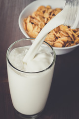 milk pouring into glass and bowl with cornflakes on the table