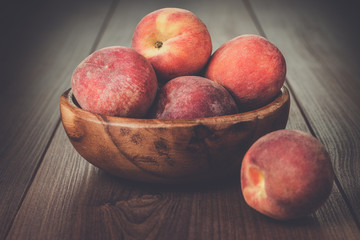 wooden bowl with some peaches on brown table