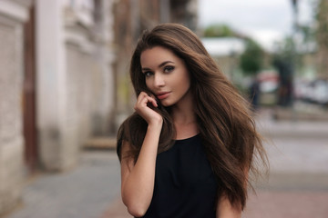 Fashion style portrait of young beautiful elegant woman in black dress walking at city streets on a...