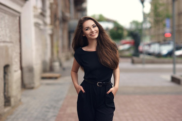 Fashion style portrait of young happy smiling beautiful elegant woman in black dress walking at...
