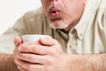 Cropped head and shoulders of man blowing into cup