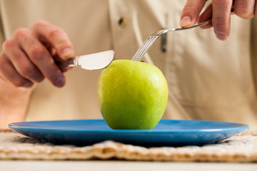 Knife and fork slicing apple over blue plate