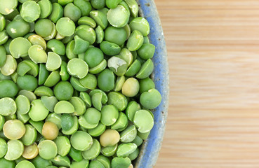 Bowl of organic green split peas on wood table top close view.