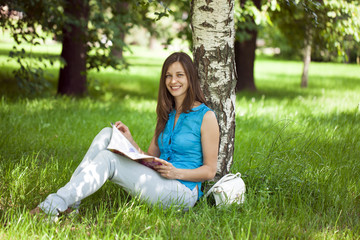 Happy woman leafing through a magazine while sitting in the summ