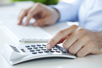 Calculating expenses. Close-up of financial businessman calculating tax expenses while sitting at...