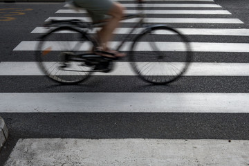 Fototapeta na wymiar Ciclista sulla bicicletta che pedala per le strade cittadine sulle strisce pedonali 