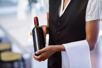 Mid section of waitress holding a bottle of red wine and a towel