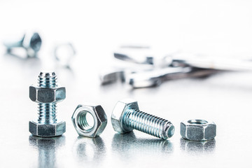 Schrauben, Muttern in Reihe und Schraubenschl&uuml;ssel auf spiegelnder Edelstahlplatte als Panorama