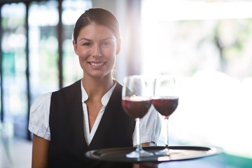 Smiling waitress holding a tray with glasses of red wine