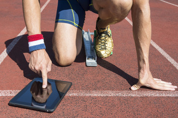 American athlete in gold running shoes crouching at the starting line of a running track wearing...