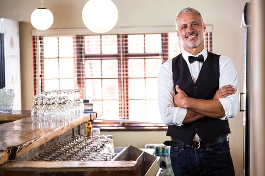 Portrait of smiling bartender standing with arms crossed