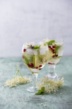 Glass of elder punch with lime, pomegranate seed and lemon balm