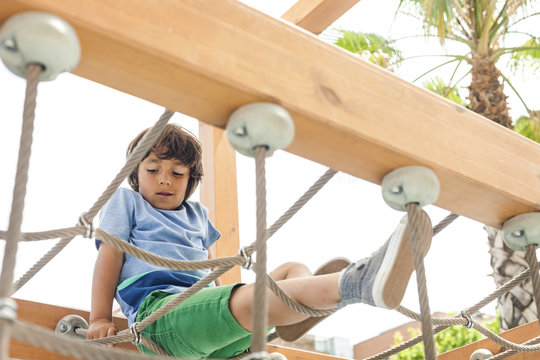 Little boy climbing on hanging bridge of a playground