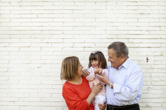 Grandparents with their granddaughter in front of white brick wall
