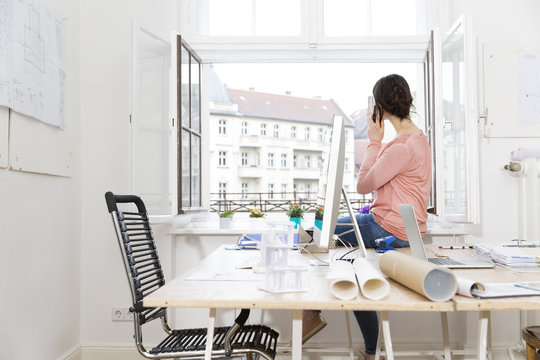 Woman in office sitting on table telephoning