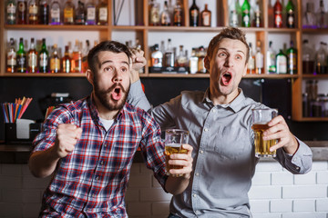 Young people with beer watching football in a bar