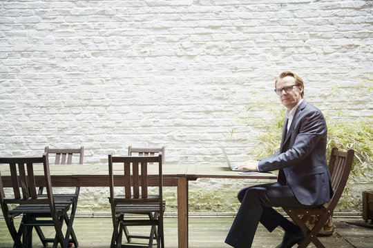 Businessman sitting at table in a backyard working with laptop