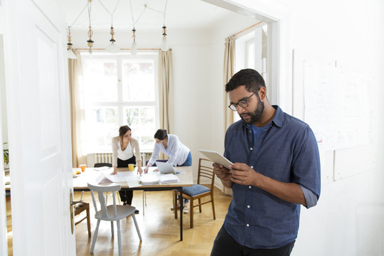 Man in office using tablet with colleagues in background