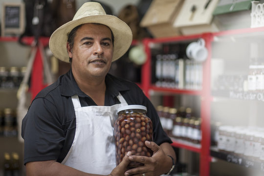 Shopkeeper in shop holding a jar with olives
